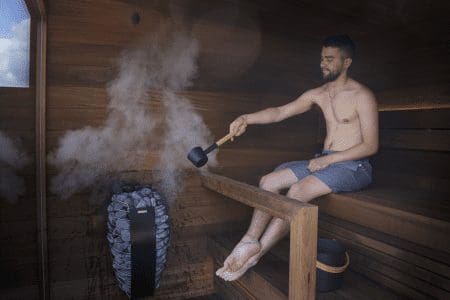 A man is sitting in the sauna with an axe.